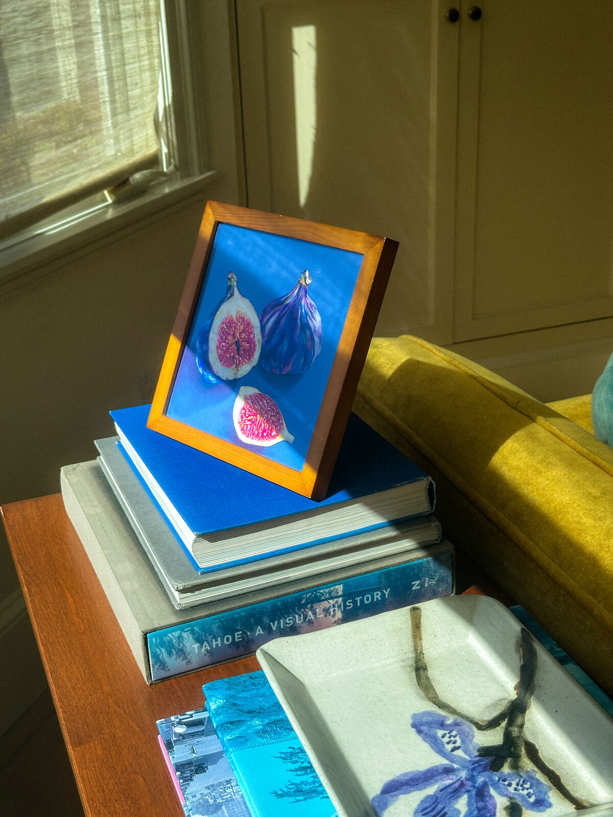 A framed Fruit Stand fig print in morning light on a stack of books