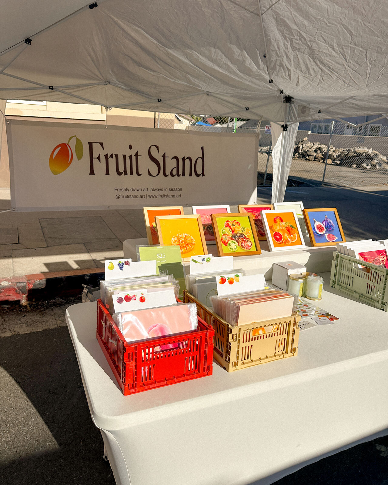 The real Fruit Stand booth at a farmers market, with the banner, framed prints and crates